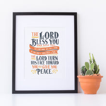 Load image into Gallery viewer, Artwork in a black frame with the with a white matte. The frame is leaning on a white counter with a terracota pot with a catcus next to it. The artwork features hand drawn lettering of the Bible verse Numbers 6:24-26 reading &quot;The Lord bless you and keep you. The Lord make his face to shine on you and be gracious to you. The Lord turn his face toward you and give you peace.&quot;