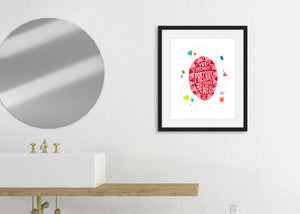 Artwork in a black frame featured in a bathroom next to a circle mirror and above a sink. The artwork features an illustrated jewel with the words inside "You are more precious than jewels." There is a scattering of illustrated, colored jewels around the image. 