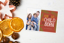 Load image into Gallery viewer, A photo of a one-sided Christmas photo card showing the front and back of the card laying on a white surface. Left of the card is a cookie cutter, pinecone, nuts and dried oranges. The photo card features one photo on the left side and on the right side the design is featured with a red background with the words “For to us a child is born, The Thompsons” with green illustrated leaves around the words.
