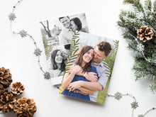 Load image into Gallery viewer, A photo of a double-sided Christmas card showing the front and back of the card laying on a white surface. Around the two sides of the card are pine cones, pine needles and a string of silver snowflake garland. The front of the card features a photo and the words “Comfort in Joy, The Thompsons” in white over the photo. The back of the card features two photos.