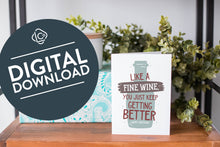 Load image into Gallery viewer, A greeting card is on a table top with a present in blue wrapping paper in the background. On top of the present is a candle and some greenery from a plant too. The card features the words &quot;Like a fine wine, you keep getting better, Happy Birthday!” with an illustration of a wine bottle behind the words. The words &quot;digital download&quot; are featured in a circle on top of the image. 