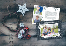 Load image into Gallery viewer, A photo of a Christmas card showing the front and back of the card laying on a wood surface. To the left of the cards are some ornaments. The front of the card features a photo with a frame around it with illustrated snowflakes. Above the photo reads “Merry Christmas” and below the photo you can add your family name. The back of the card features two photos, illustrated snowflakes and a place to add a family update.
