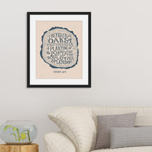 Artwork in a black frame with the with a white matte shown hanging on a wall above a sofa. The artwork features an illustration of a wood log outline with the words "They will be oaks of righteousness, a planting of the Lord for the display of his splendor."