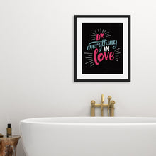 Load image into Gallery viewer, A black art print in a black frame hangs on a white bathroom wall. Below it is a freestanding white bath with brass taps.  The print reads &quot;Do everything in love&quot; in bright pink and blue hand-lettering style, with white dashes around the words.