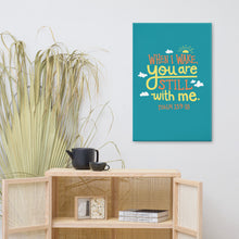 Load image into Gallery viewer, A turquoise canvas hangs on a white wall, above a rattan sideboard holding black crockery and books. The canvas reads &#39;When I wake you are still with me, Psalm 139:18&#39; in orange and yellow lettering, illustrated with a small yellow sun and little grey clouds.