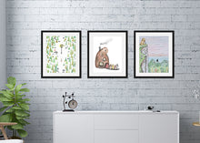 Load image into Gallery viewer, Three black frames featured in a white brick wall above a dresser. The first frame features illustrated artwork with Lucy walking to the lamp. The second frame features an illustration of the beavers house shaped like a beaver with the four children walking up to it. The third frame features a scene on a mountain top with Aslan and Peter overlooking Narnia.  