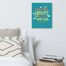 Load image into Gallery viewer, A turquoise canvas hangs on a white bedroom wall, above a white bed covered with gery and white pillows, and a small wooden table holding books. The canvas reads &#39;When I wake you are still with me, Psalm 139:18&#39; in orange and yellow lettering, illustrated with a small yellow sun and little grey clouds.