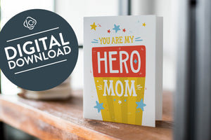 A card on a wood tabletop with an object in the background that is out of focus. The card features the words “You are my hero mom.” The words "digital download" are featured in a circle on top of the image. 