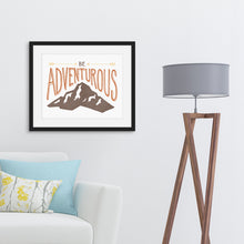 Load image into Gallery viewer, A black frame hanging on the wall above a sofa. The lettering and illustration says “Be adventurous” with arrows pointing to the word “be” and a brown mountain illustration underneath the word “adventure.”