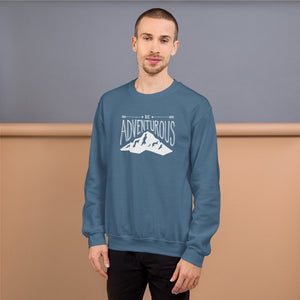 A man wearing an indigo blue hoodie with lettering and illustration in white with the phrase “Be Adventurous” with arrows pointing to the word “be” and a mountain illustration underneath the word “adventure.”