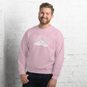 A man wearing a light pink hoodie with lettering and illustration in white with the phrase “Be Adventurous” with arrows pointing to the word “be” and a mountain illustration underneath the word “adventure.”