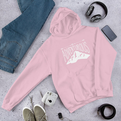 A light pink hooded sweatshirt laying with jeans and shoes. The pink hoodie includes the phrase “Be Adventurous” in white with arrows pointing to the word “be” and a mountain illustration underneath the word “adventure.”