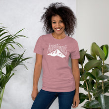 Load image into Gallery viewer, A woman wearing an orchid pink short sleeved t-shirt. The tee features the lettering and illustration in white. The phrase “Be adventurous” with arrows pointing to the word “be” and a mountain illustration underneath the word “adventure.”