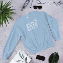 Load image into Gallery viewer, A light blue sweatshirt laying on the ground with objects around it. The sweatshirt features hand drawn lettering in white with the words &quot;May the God of hope fill you with all joy and peace as you trust him.&quot;