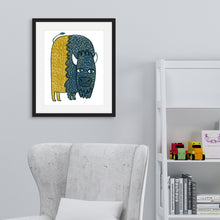 Load image into Gallery viewer, A black frame on a wall featured in a nursery with a sitting chair and shelf. The frame features illustrated artwork of a buffalo in blue and yellow. 