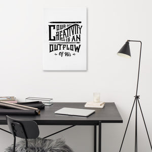 A canvas on a wall above a desk. The canvas is white and features hand drawn lettering featuring "Our creativity is an outflow of His." The lettering is in black. 