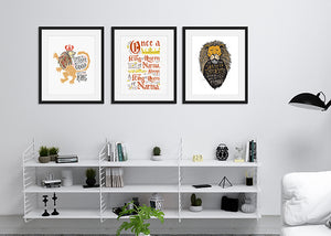 Three black frames on a wall above a shelf. Frame one features a lion's head illustration of Aslan with the quote "At The Sound of Your Roar, Sorrows Will Be No More." The second frame featuring letter artwork reading "Once a king or queen of Narnia, always a king or queen of Narnia." The third frame has an illustration of a lion saying "Course He Isn't Safe, But He's Good. He's the King."