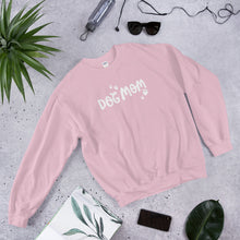 Load image into Gallery viewer, This light pink comfy sweatshirt features the words Dog Mom in the center with white, heart shaped paws surrounding the Dog Mom words. This sweatshirt makes a fun gift for dog lovers. 