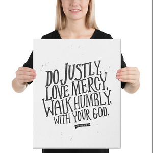 A woman holding a white canvas with black lettering with Do justly, love mercy, walk humbly, with your God, Micah 6:8.