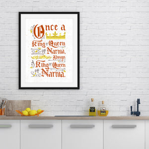 A black frame on a white brick wall with artwork in it. The frame is above a kitchen counter. The artwork features hand drawn lettering of the Narnia quote "Once a king or queen of Narnia, always a king or queen of Narnia." 