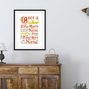 A black frame above a wood credenza with artwork inside of the frame. The artwork features hand drawn lettering of the Narnia quote "Once a king or queen of Narnia, always a king or queen of Narnia."