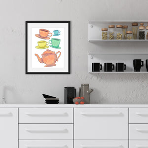 A black frame is hanging on a stucco kitchen wall above a kitchen counter and next to some shelves. The white shelves have clear containers of pasta and the bottom shelf has tea mugs. The counter has a tea pot and plates on it. The frame has artwork on a white background with four teacups on saucers and one large teapot. The teacups are in muted colors of orange, blue, yellow and green and the teapot is a muted orange. On the teacups, saucers and teapot there is a light flower detail pattern.