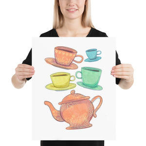 A woman is holding a paper art print in her hands. The artwork is on a white background with four teacups on saucers and one large teapot. The teacups are in muted colors of orange, blue, yellow and green and the teapot is a muted orange. On the teacups, saucers and teapot there is a light flower detail pattern.