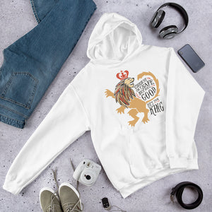A white hoodie laying on the ground with objects around it. The hoodie features hand drawn illustration of the Chronicles of Narnia lion character Aslan. Inside the illustration there is the quote "Course He Isn't Safe, But He's Good. He's the King."