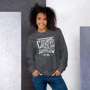 A woman wearing a dark grey sweatshirt featuring hand drawn lettering in white with the words "Our creativity is an outflow of His."