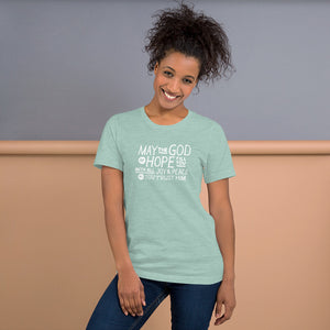 A woman wearing a heather prism dusty blue color short sleeved t-shirt. The t-shirt features hand drawn lettering in white with the words "May the God of hope fill you with all joy and peace as you trust him."