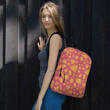 Load image into Gallery viewer, A woman standing by a black fence with one hand on the fence. She is turned sideways with a backpack over one arm. The backpack features illustrated gems and diamonds in gold on top off a muted hot pink colored backpack. 