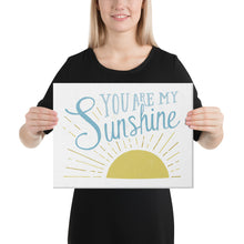 Load image into Gallery viewer, A woman is holding up a white canvas and smiling. The canvasreads &#39;You are my sunshine&#39; in blue over a yellow sun illustration