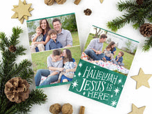 Load image into Gallery viewer, A photo of a two-sided Christmas card showing the front of the card on top of a brown wrapped gift on a white tabletop. Around the gift are pine needles, pinecones and wood star ornaments. The front of the card features a photo on the top and on the bottom is in green with words in white “Hallelujah Jesus is Here” with white stars around it. The back of the card features two photos. 
