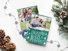 Load image into Gallery viewer, A photo of a double-sided Christmas card showing the front and back of the card laying on a white surface. Around the two sides of the card are pine cones, pine needles and a string of silver snowflake garland. The front of the card features a photo on the top and on the bottom is in green with words in white “Hallelujah Jesus is Here” with white stars around it. The back of the card features two photos.