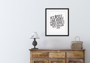 Artwork is featured hanging above a wood dresser with a lamp and basket on top of it. The artwork features hand drawn lettering reading "Act Justly, Love Mercy, Walk Humbly with your God" - Micah 6:8.