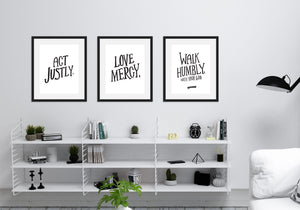 Three black frames featured above a shelving unit in a living room. The first frame features artwork saying "Act Justly." The second frame says "Love Mercy." The third frames says "Walk Humbly, with your God - Micah 6:8."