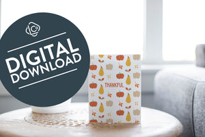 A greeting card is featured on round coffee table with a green plant and sofa in the background. The card features the word "Thankful" with a pattern of illustrated pumpkins and leaves behind the word. The words "digital download" are featured in a circle over the image.