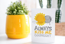 Load image into Gallery viewer, A greeting card is on a table top with a yellow plant pot and a green plant inside. The card features the words “Always kiss me goodnight” with an illustrated sun and moon giving each other a kiss.