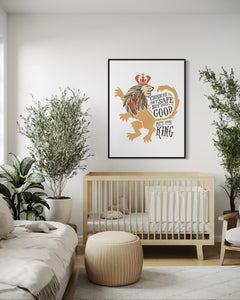 Artwork in a black frame with the with a white matte. The frame is hanging on a wall in a nursery above a crib. The artwork features an illustrated with the words "Course He Isn't Safe, But He's Good. He's the King."