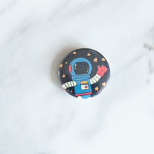 Load image into Gallery viewer, A button on a white tabletop. The button features space-themed illustration of an astronaut. 