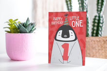 Load image into Gallery viewer, A greeting card standing up on a table with a plant in a pink pot behind it. The card features an illustrated penguin with a party hat on and holding the number one and reads &quot;Happy birthday little one.&quot;