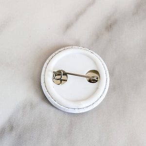 A button pin on a white table showing the back metal clasp of the button. 