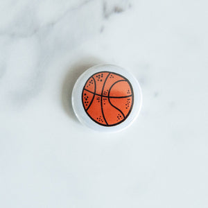 A buttons on a white tabletop. The button features an illustrations of a basketball. 