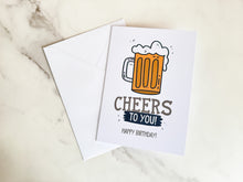 Load image into Gallery viewer, A greeting card with a white envelope laying on a tabletop. The card features the words “Cheers to you, happy birthday” with an illustrated beer mug.