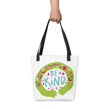 Load image into Gallery viewer, Someone holding a white tote bag with black handle. The bag features a design with the words &#39;be kind&#39; with illustrated hugging hands around the words. 