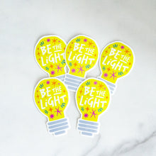 Load image into Gallery viewer, Five die cut vinyl stickers with the words &quot;be the light&quot; inside an illustrated lightbulb.