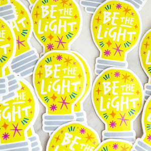 Die cut vinyl stickers with the words "be the light" inside an illustrated lightbulb.