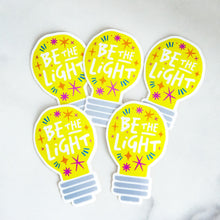 Load image into Gallery viewer, Die cut vinyl stickers with the words &quot;be the light&quot; inside an illustrated lightbulb.