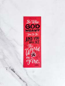 A bookmark on a marble tabletop with a orange/red backround and the words "Be who God meant you to be and you will set the world on fire."