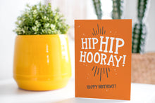 Load image into Gallery viewer, A greeting card is on a table top with a yellow plant pot and a green plant inside. The card features the words “Hip Hip Hooray, Happy Birthday.”